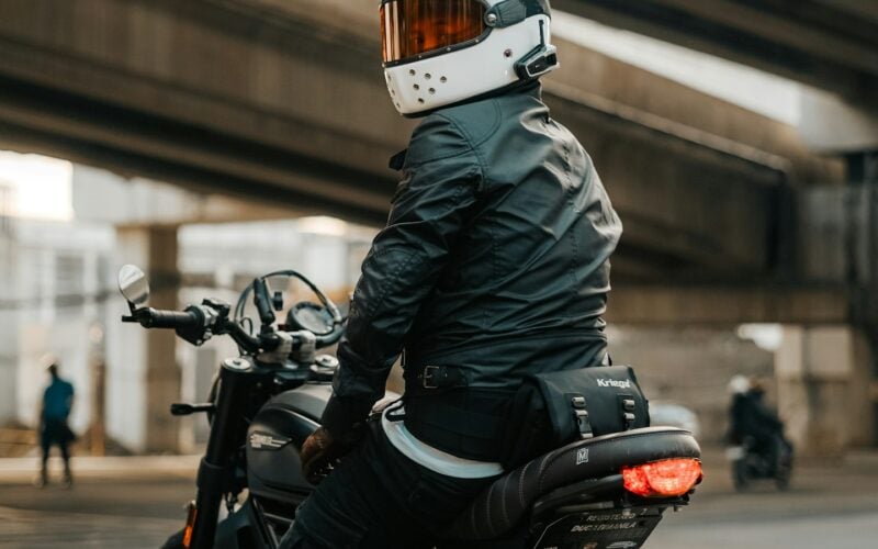 A motorcyclist seen from behind wearing a textile riding jacket, gloves and a full-face helmet (photo: Kristian Angelo / Unsplash)