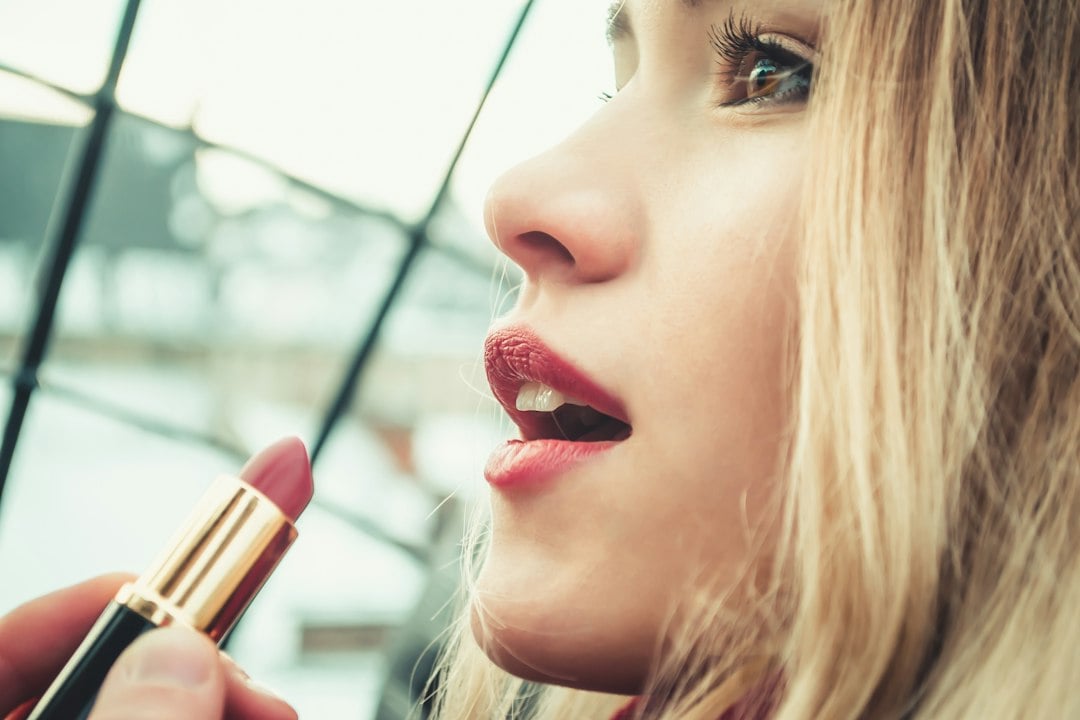 Close-up of a woman applying lipstick from a gold tube.