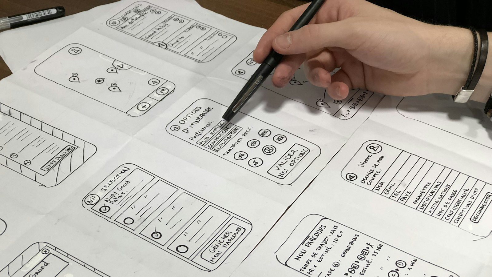 A hand with a black pen sketching phone-sized page layouts on large sheets of paper (photo: Amélie Mourichon / Unsplash)