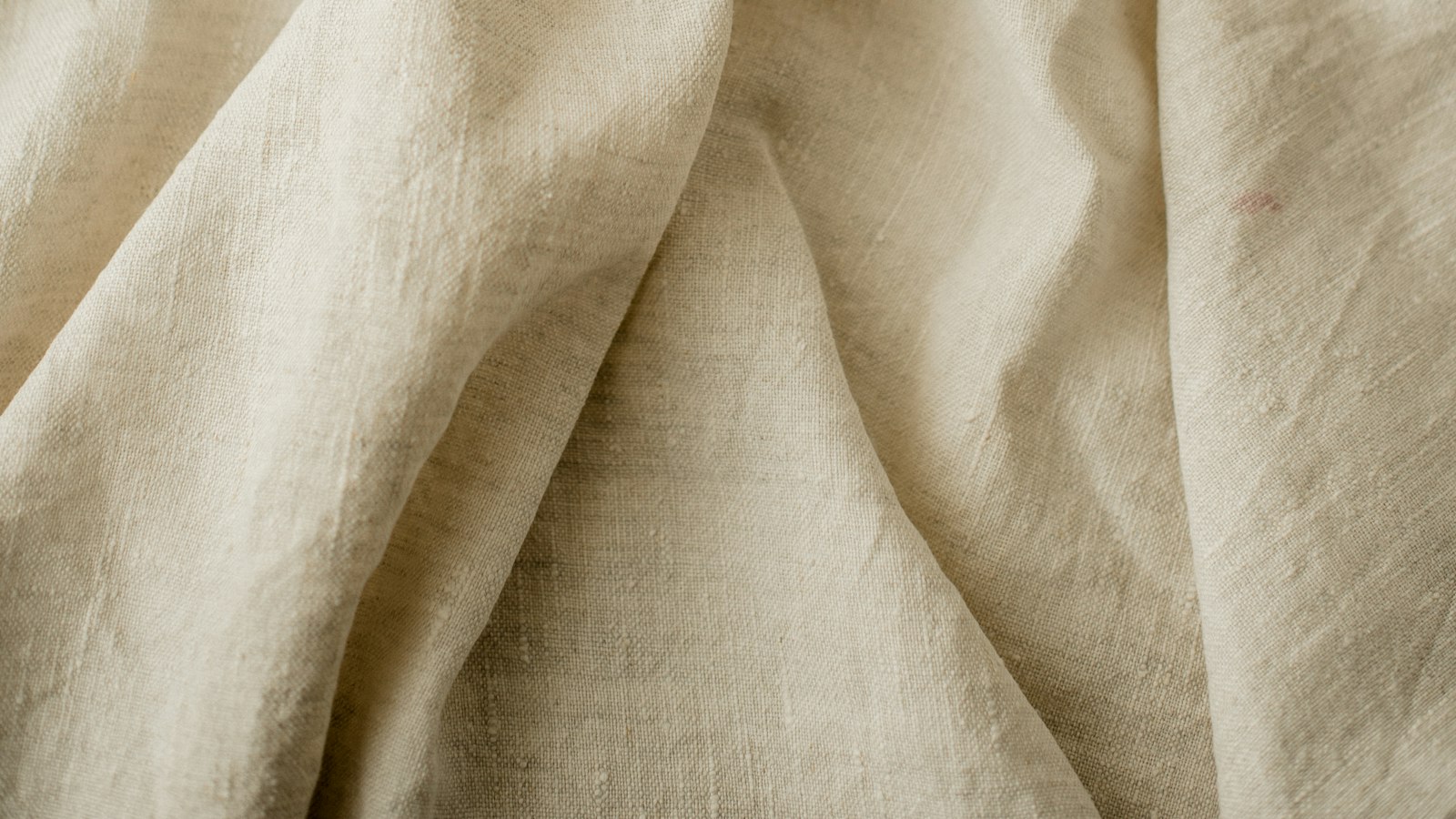 Close view of the soft folds of undyed linen bedding catching daylight