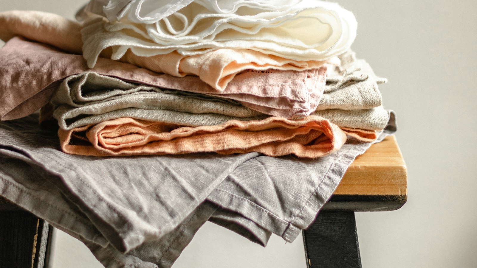 A pile of folded cloths and linens in cream, pink and grey, showing different weaves and weights