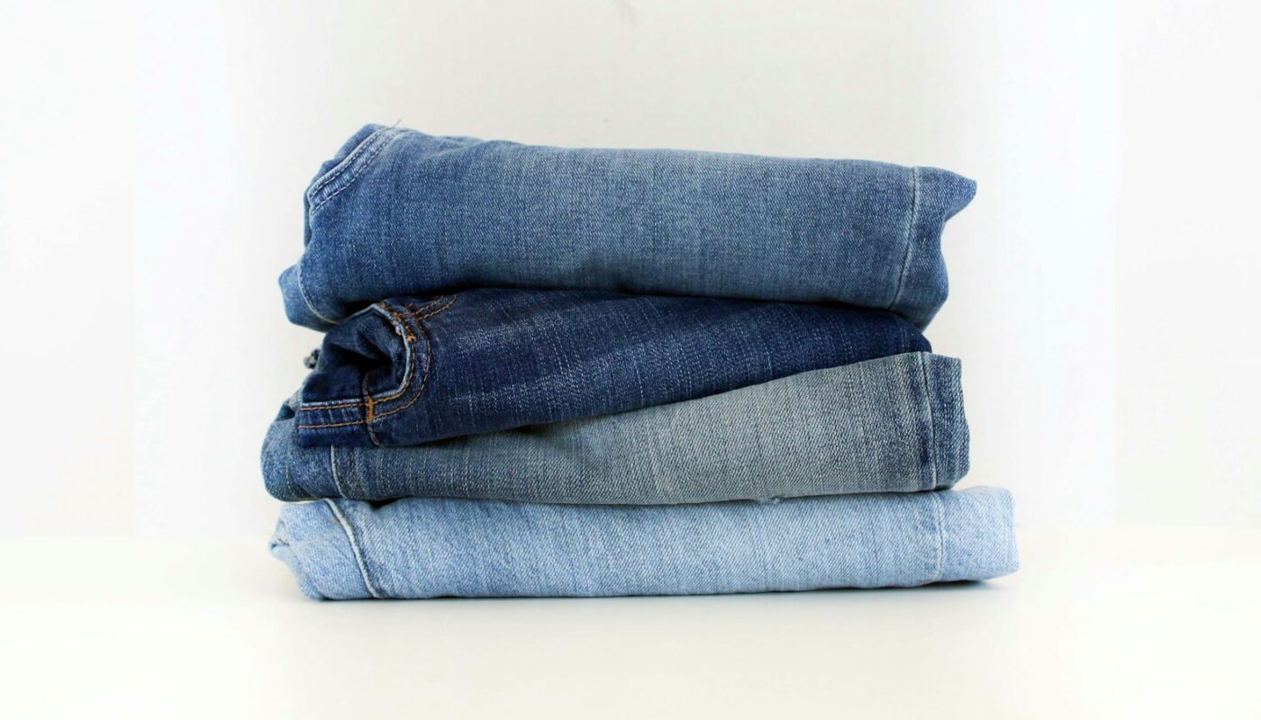 A stack of four folded pairs of jeans running from dark indigo to pale light wash (photo: Claire Abdo / Unsplash)