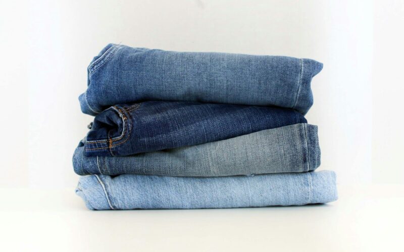A stack of four folded pairs of jeans running from dark indigo to pale light wash (photo: Claire Abdo / Unsplash)