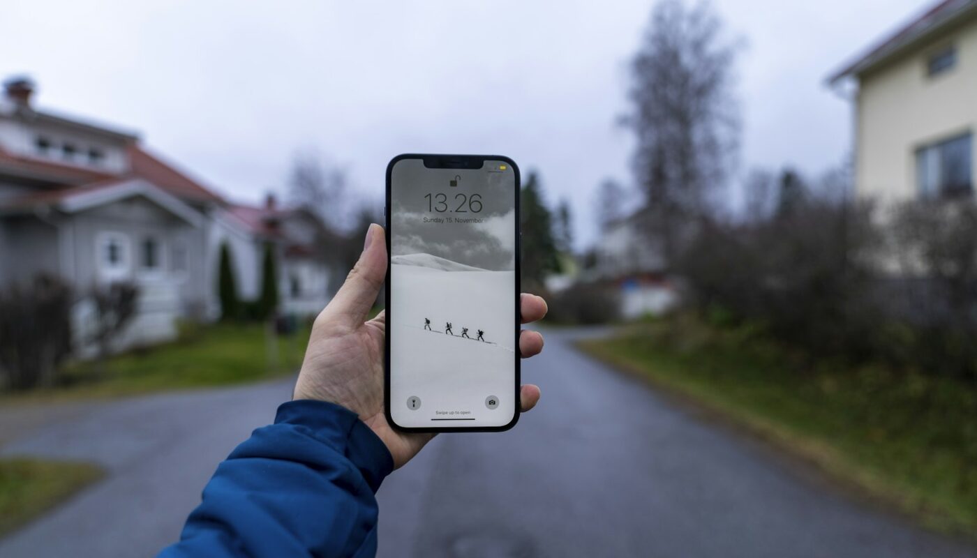 A hand holding a smartphone on a quiet residential street (photo: Hendrik Morkel / Unsplash)