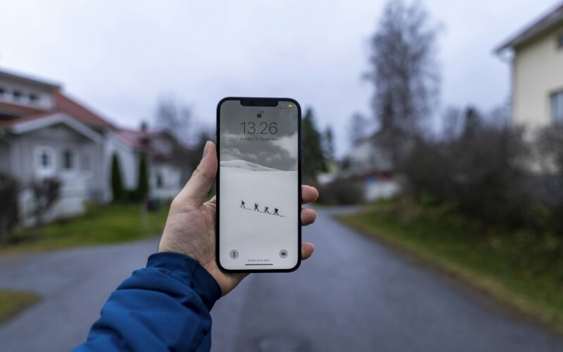 A hand holding a smartphone on a quiet residential street (photo: Hendrik Morkel / Unsplash)