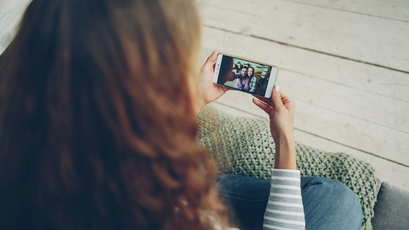 A woman on a sofa on a video call on her phone (photo: Vitaly Gariev / Unsplash)