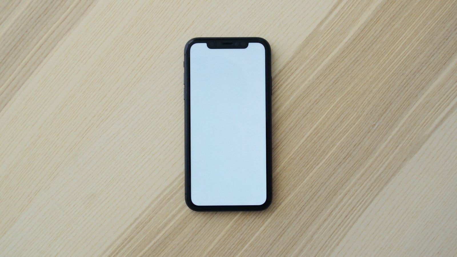 A smartphone lying on a light wooden table (photo: Vojtech Bruzek / Unsplash)