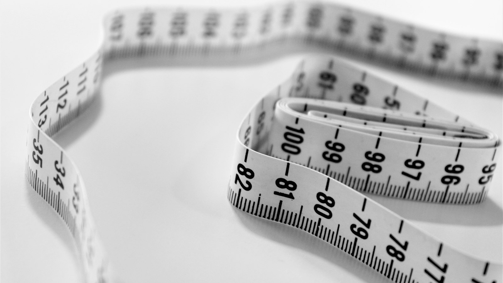 A soft tailor’s tape measure coiled on a white surface showing centimetre markings (photo: Siora Photography / Unsplash)