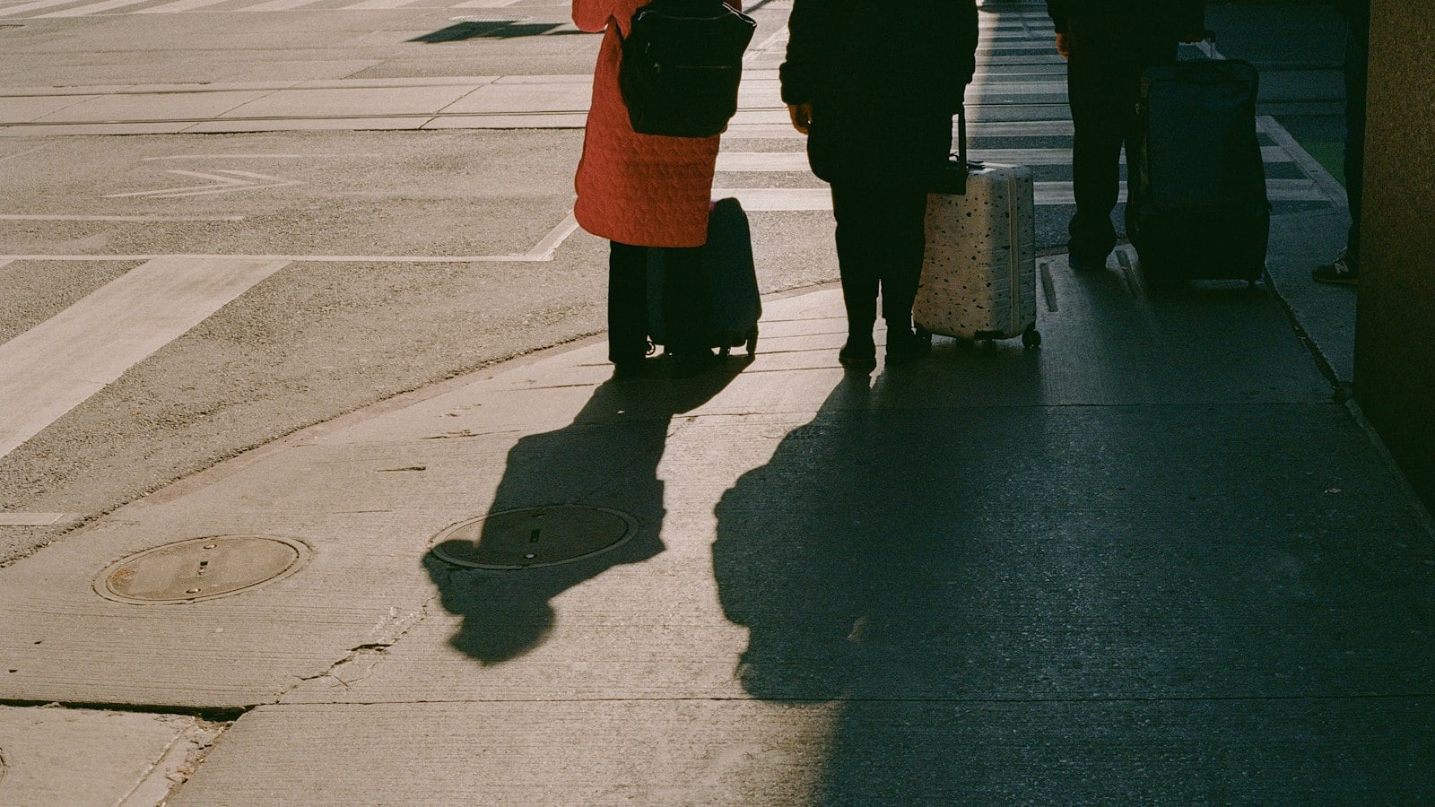 Travellers pulling suitcases along a pavement, casting long shadows in low sunlight (photo: Jim Luo / Unsplash)