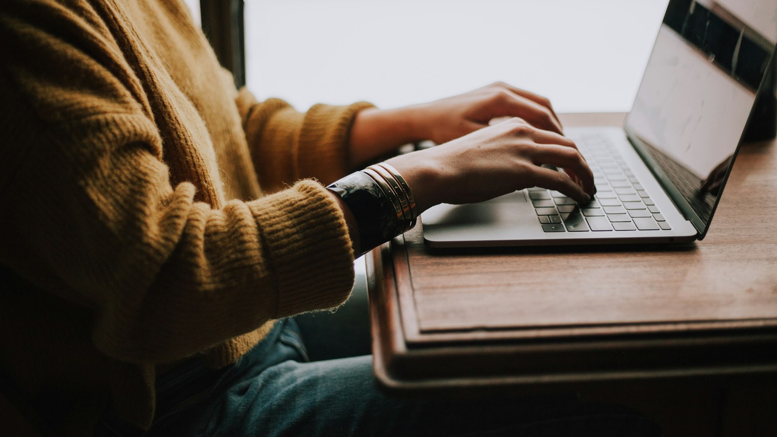 A person in a mustard sweater typing on a laptop (photo: Christin Hume / Unsplash)