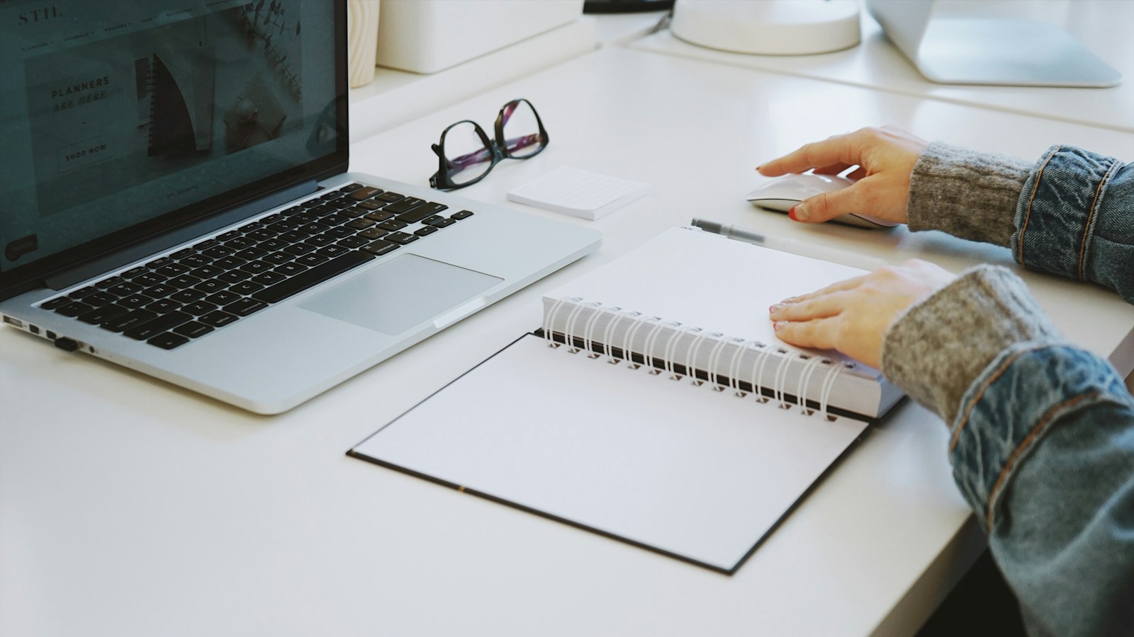 A laptop and an open notebook on a white desk (photo: Marissa Grootes / Unsplash)