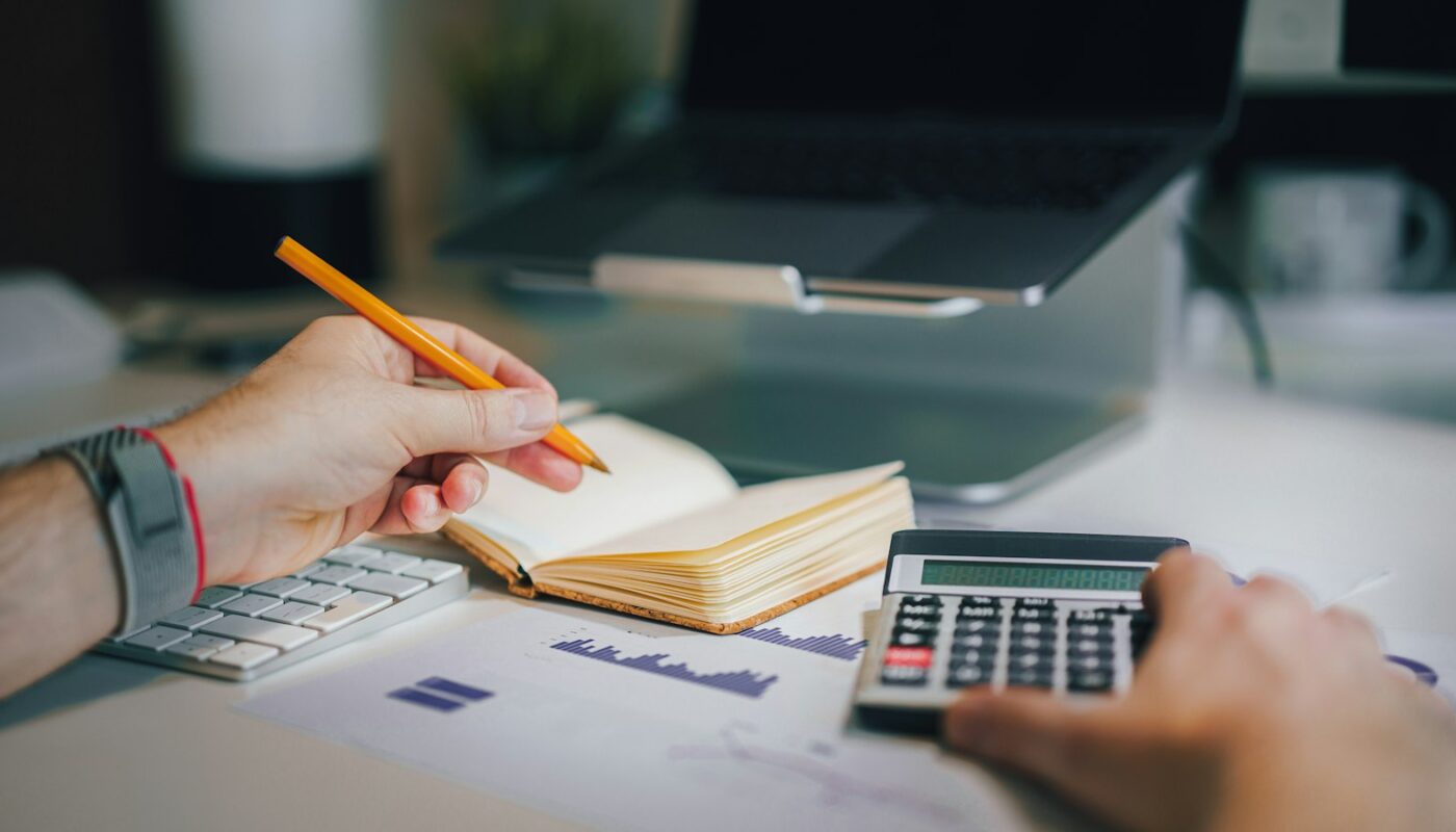 Person working out a budget with a calculator and notebook (photo: Jakub Żerdzicki / Unsplash)