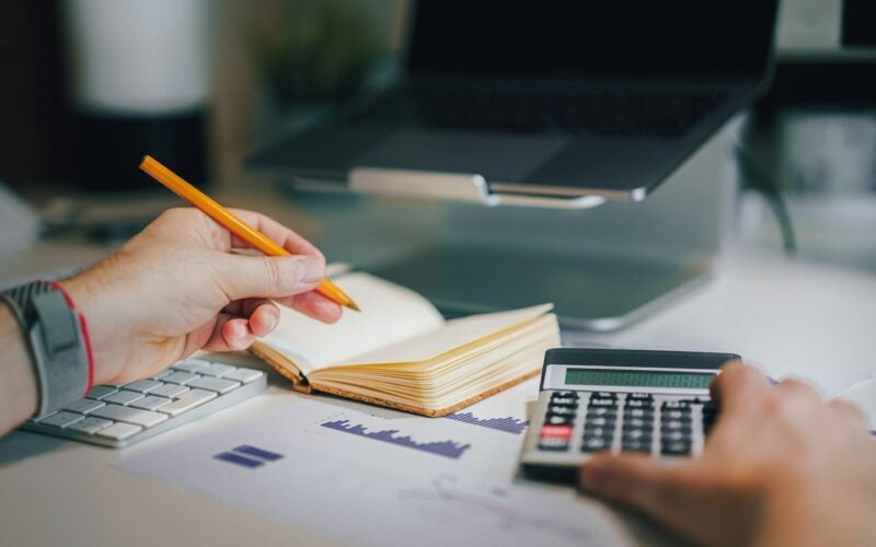 Person working out a budget with a calculator and notebook (photo: Jakub Żerdzicki / Unsplash)