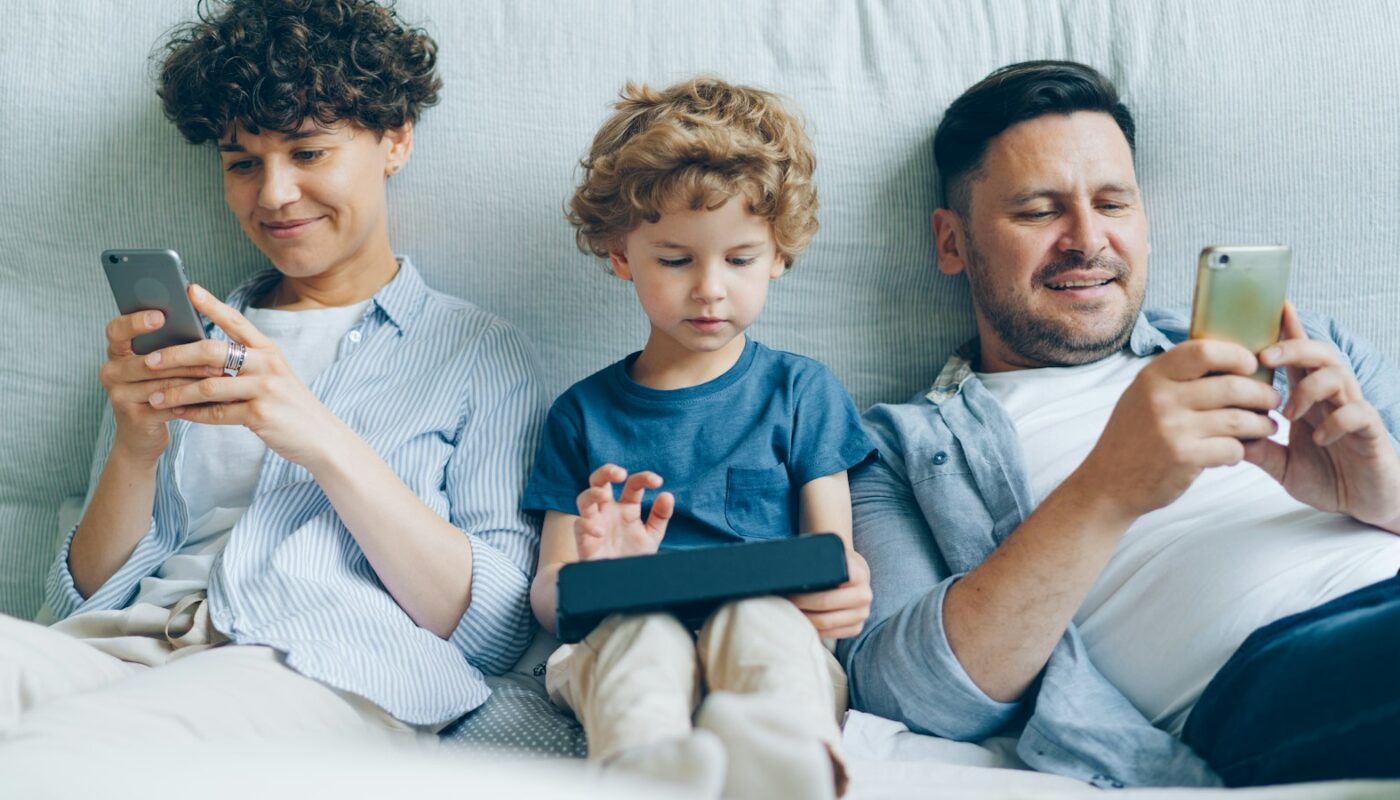 A family on a sofa using phones and a tablet (photo: Vitaly Gariev / Unsplash)