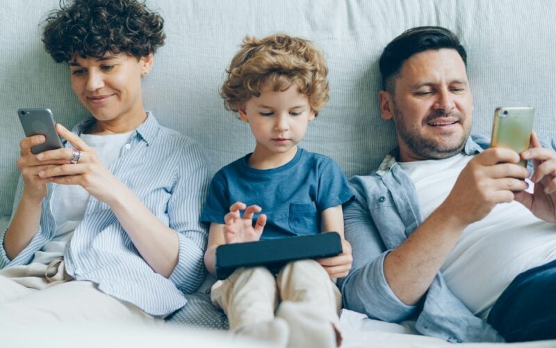 A family on a sofa using phones and a tablet (photo: Vitaly Gariev / Unsplash)