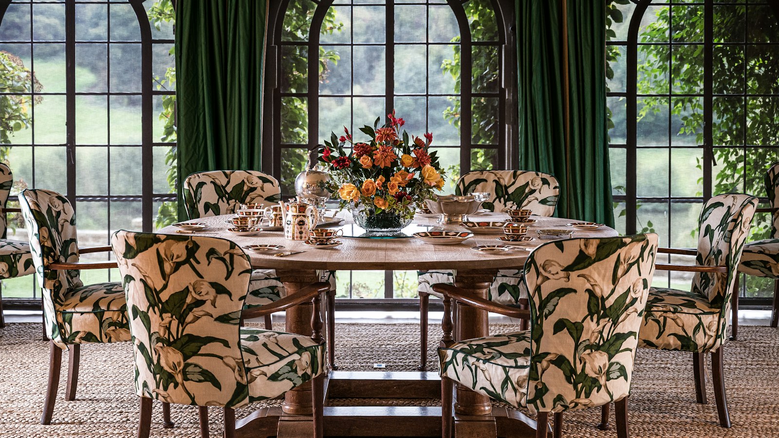 A round dining table with patterned upholstered chairs beneath arched windows (photo: Jez Timms / Unsplash)