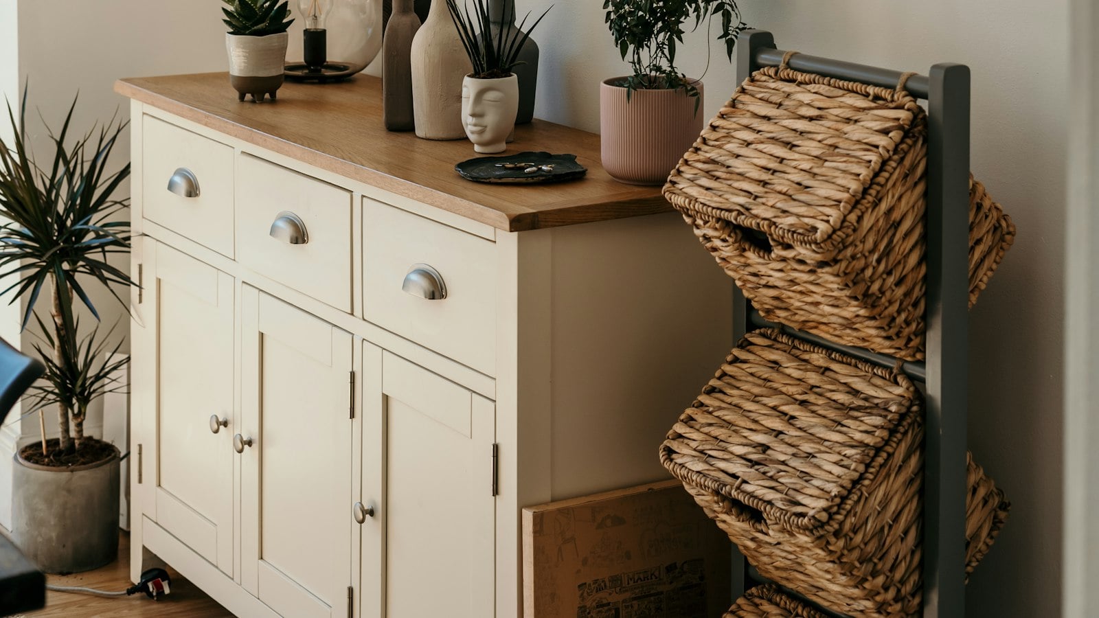 A wooden sideboard styled with plants, vases and a woven basket (photo: Toa Heftiba / Unsplash)