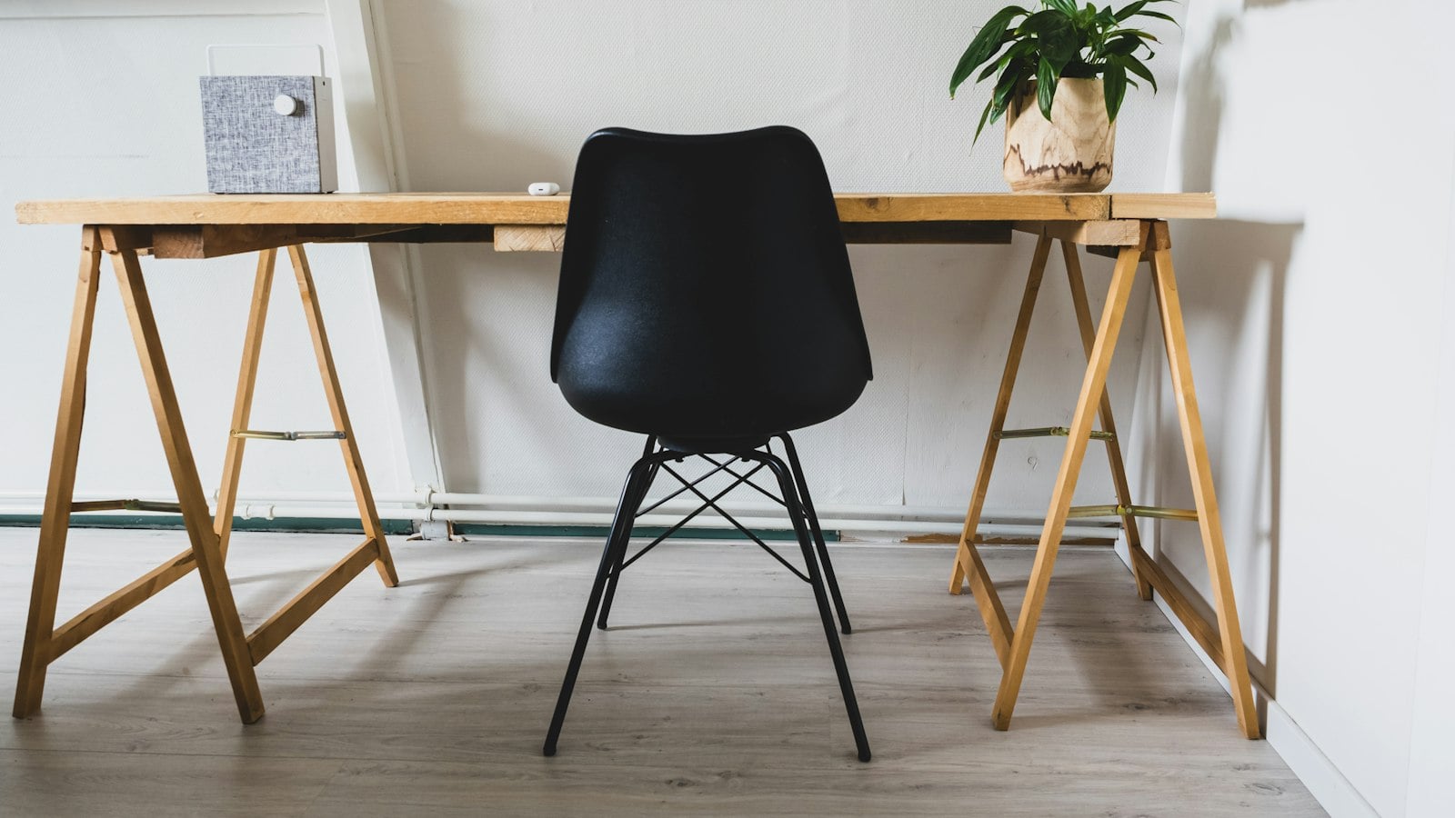 A simple wooden trestle desk with a black chair and a plant (photo: Sven Brandsma / Unsplash)