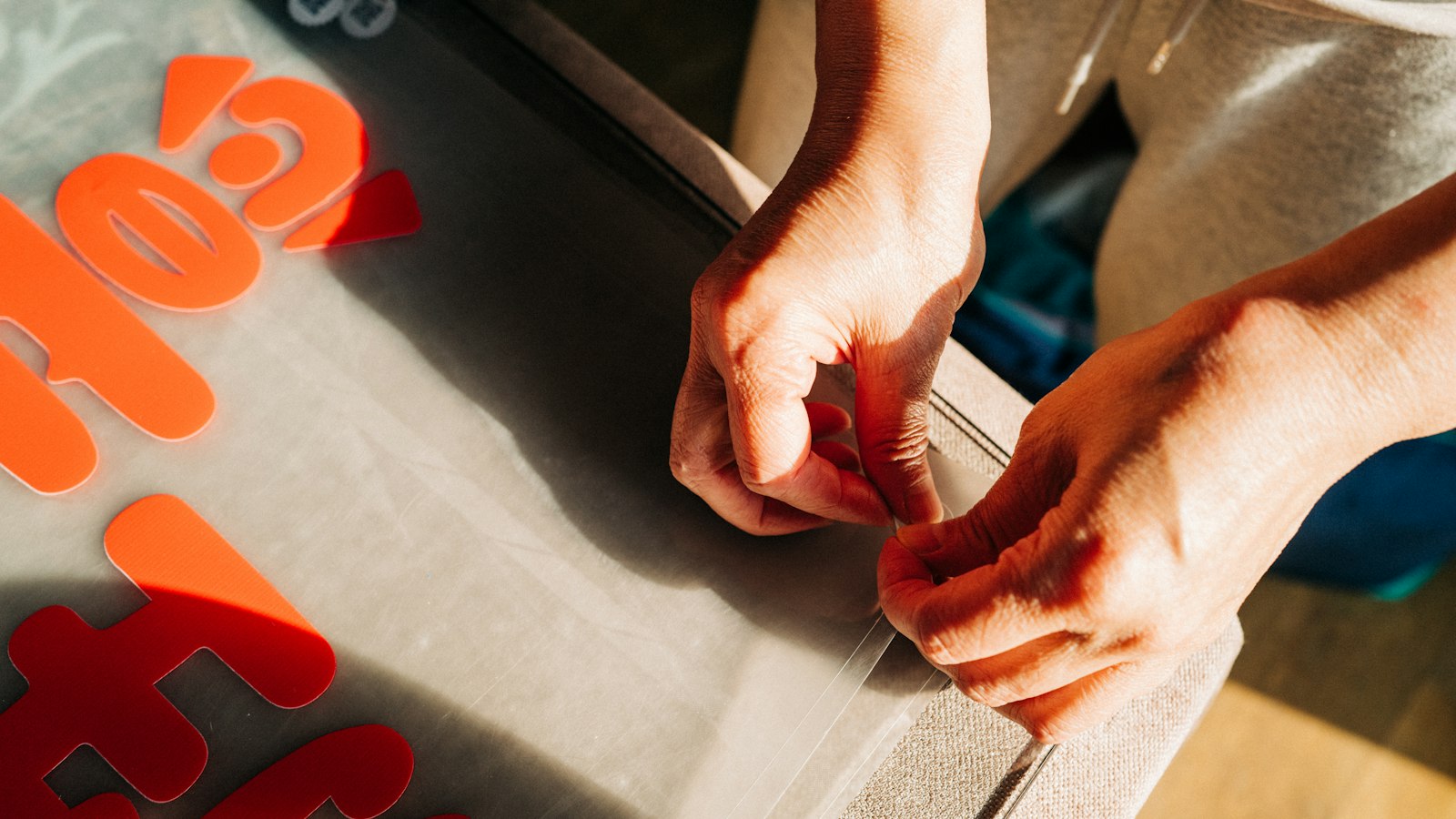 Hands peeling away the excess from cut orange vinyl lettering on its backing sheet (photo: Steve Long / Unsplash)