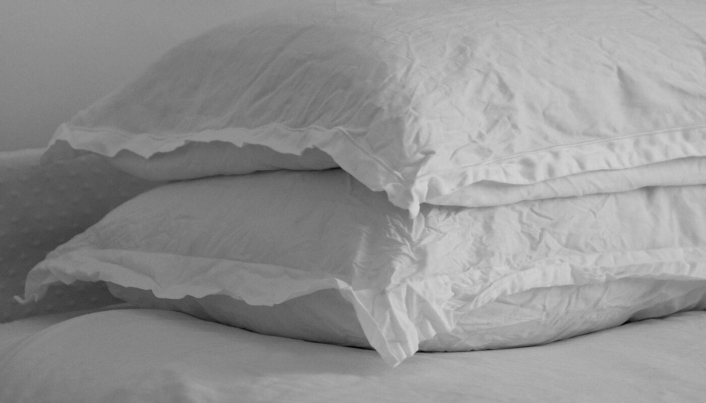 Two white pillows stacked on a made bed (photo: the blowup / Unsplash)