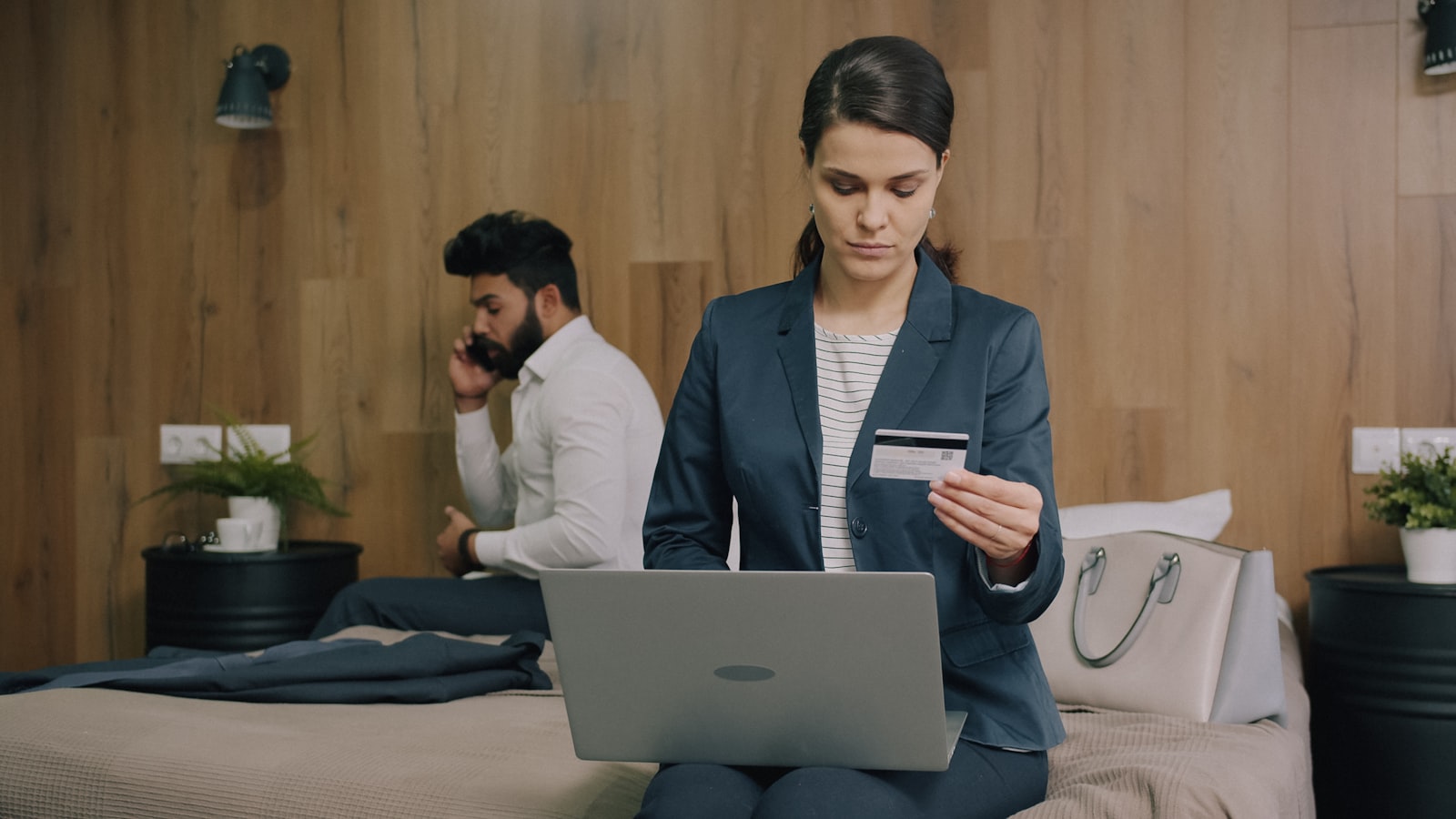 A woman in a blazer holding a payment card while using a laptop (photo: Vitaly Gariev / Unsplash)