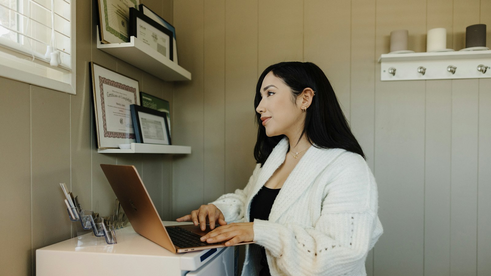 A woman in a cream cardigan working at a laptop at a small desk in a home office (photo: Omar Lopez / Unsplash)