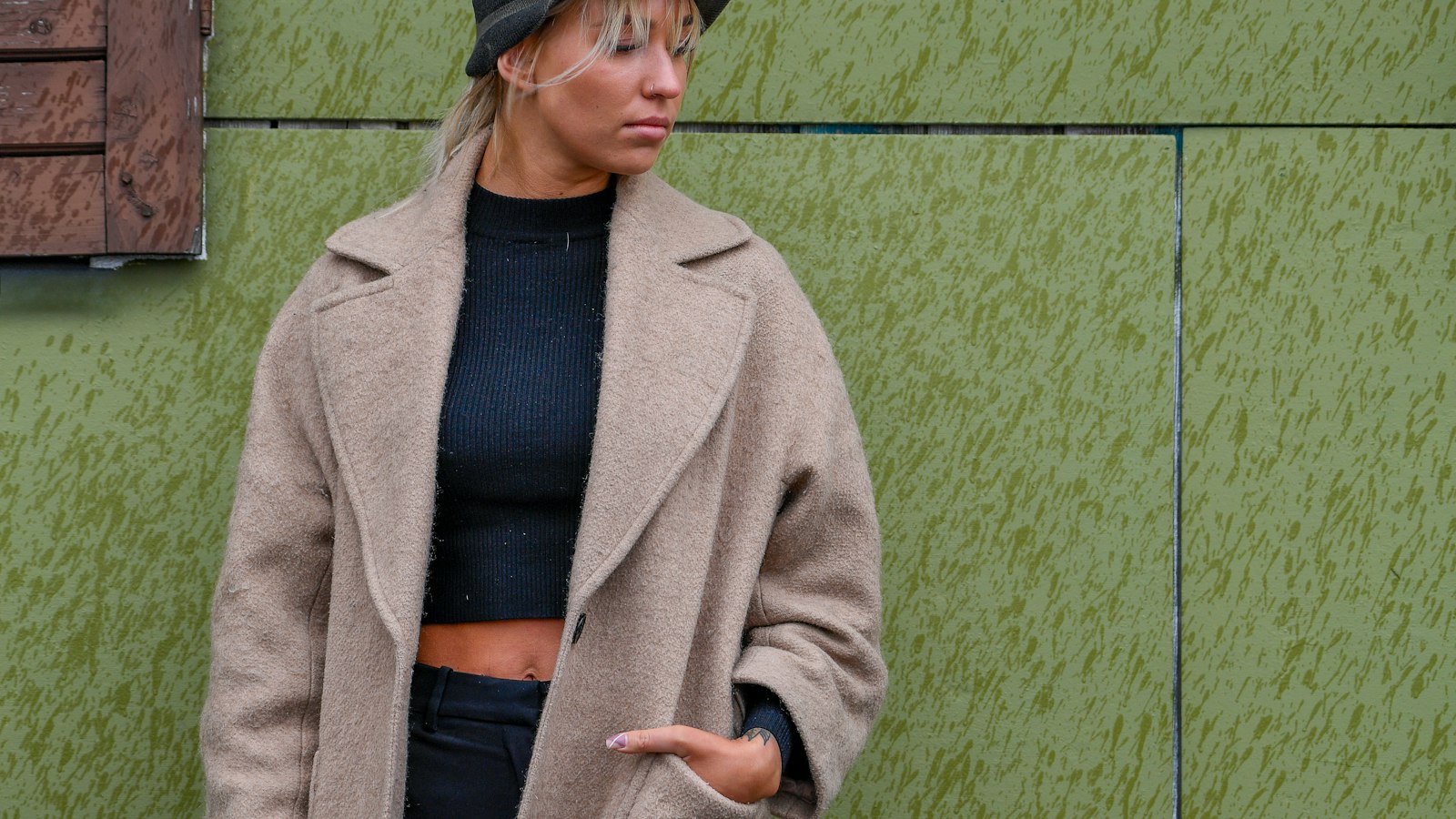 A woman in a long oatmeal wool coat against a green wall (photo: Margo Evardson / Unsplash)